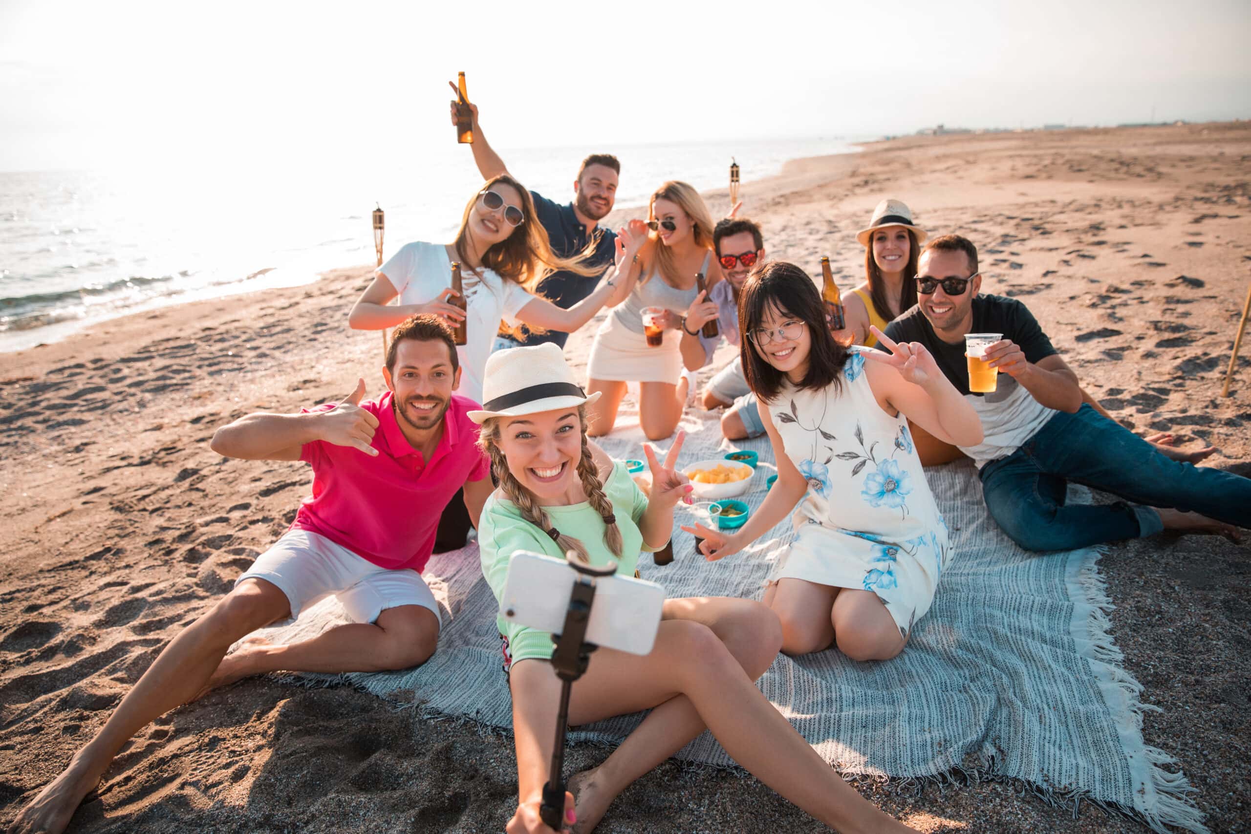 Multicultural group of friends partying on the beach – happy young people celebrating during summer vacation, summer time and holidays concepts.